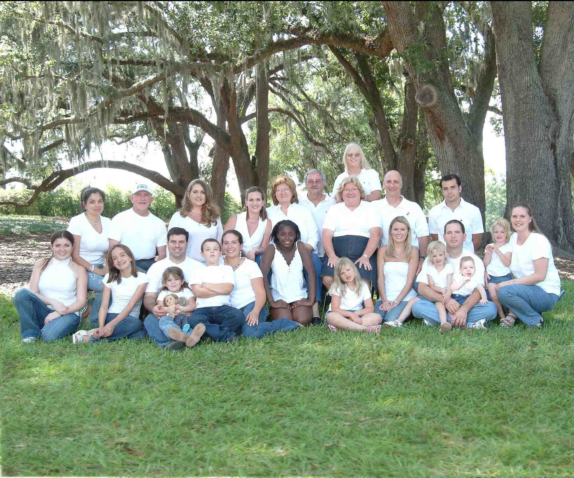 Large family portrait with 24 members all in white shirts under oak trees