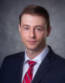 Brandon A Professional Headshot of a man, dark suit, red tie with blue and white stripes